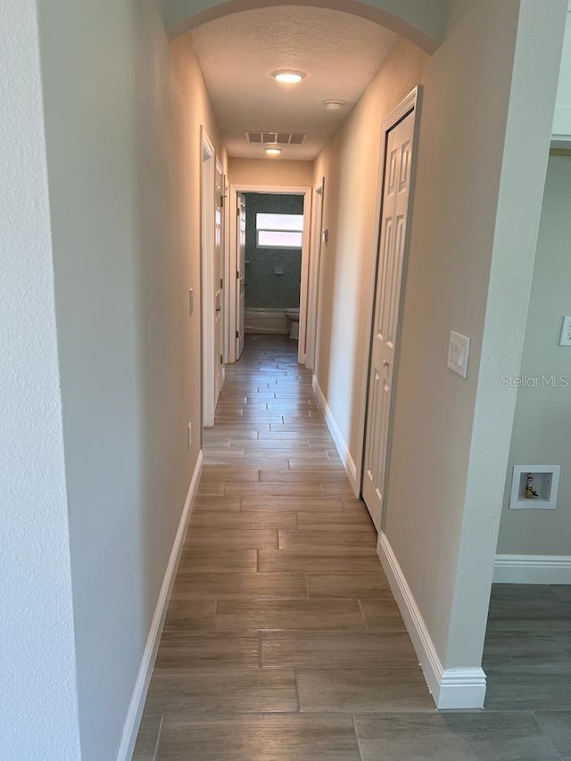hall featuring visible vents, wood finished floors, baseboards, and arched walkways