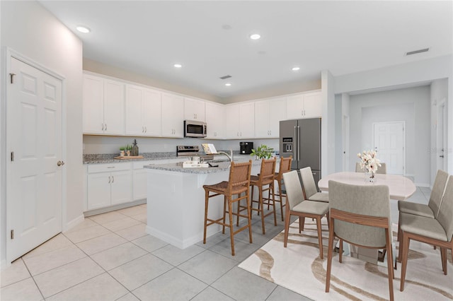 kitchen with a kitchen island with sink, a breakfast bar area, white cabinetry, light tile patterned floors, and appliances with stainless steel finishes