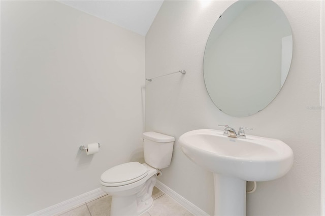 half bath featuring toilet, tile patterned flooring, a sink, and baseboards
