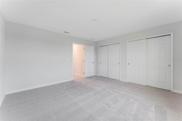 unfurnished bedroom featuring two closets, baseboards, carpet floors, and visible vents