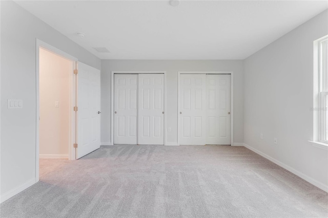 unfurnished bedroom with two closets, visible vents, baseboards, and carpet floors