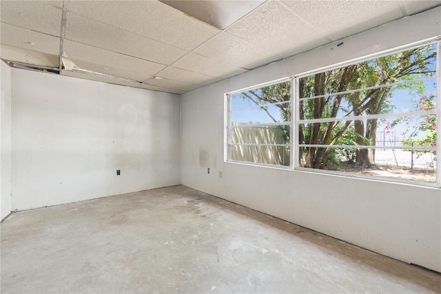 spare room with a paneled ceiling, a wealth of natural light, and unfinished concrete floors
