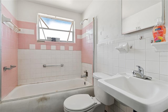 bathroom featuring a sink, toilet, tub / shower combination, and tile walls