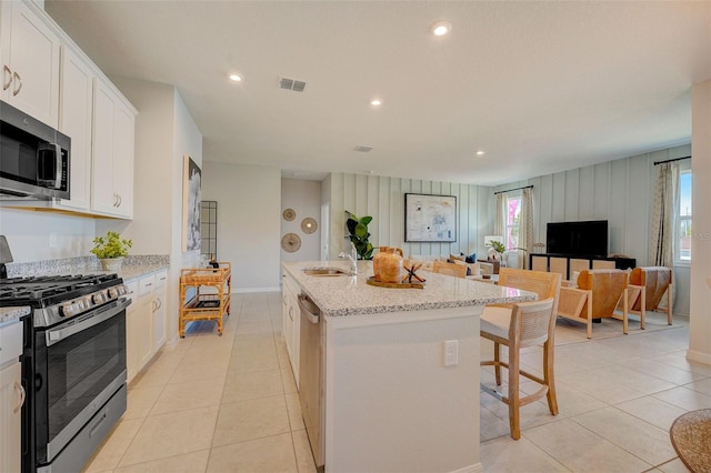 kitchen featuring an island with sink, a breakfast bar, white cabinets, visible vents, and appliances with stainless steel finishes