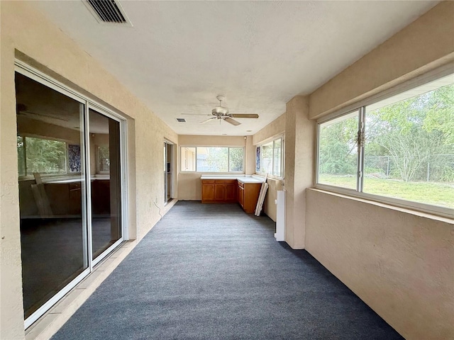 unfurnished sunroom featuring carpet flooring, visible vents, ceiling fan, and a textured wall