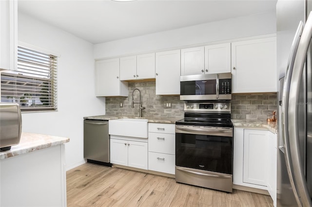1348 Myerlee Gardens Ave, Fort Myers, FL 33919 - kitchen featuring stainless steel appliances, a sink, white cabinets, light wood finished floors, and decorative backsplash