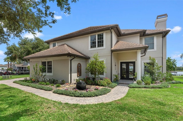 view of front of property with french doors, a chimney, a front lawn, a tiled roof, and stucco siding