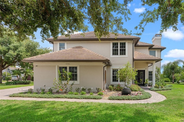 view of front of home with a chimney, stucco siding, a front yard, and a tile roof
