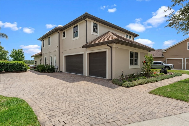 view of side of property with stucco siding, decorative driveway, and an attached garage