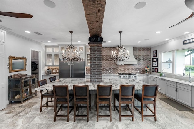 kitchen with stainless steel built in fridge, washer / dryer, a chandelier, a sink, and ornamental molding