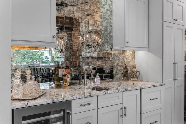 bar area featuring wine cooler, tasteful backsplash, a sink, and a chandelier