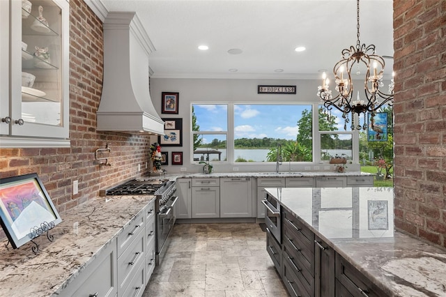 kitchen featuring high end stove, light stone counters, stone tile flooring, decorative light fixtures, and ornamental molding