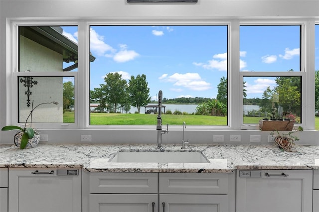 interior space with a sink, a water view, dishwasher, white cabinets, and light stone countertops