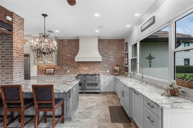 kitchen with high quality appliances, wall chimney exhaust hood, a sink, a kitchen breakfast bar, and light stone finish flooring