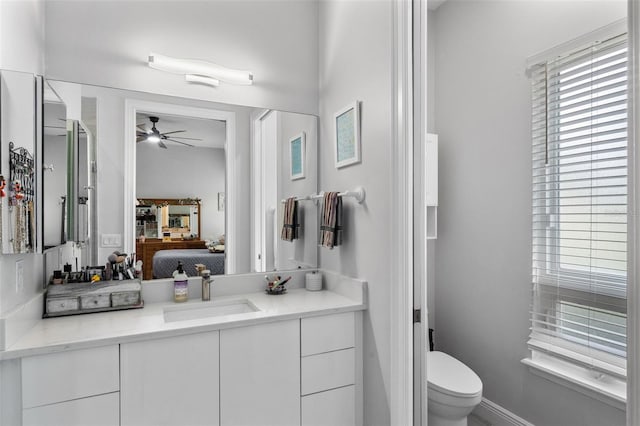 ensuite bathroom with ceiling fan, toilet, vanity, and baseboards