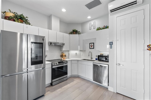 kitchen with stainless steel appliances, a sink, an AC wall unit, under cabinet range hood, and light countertops