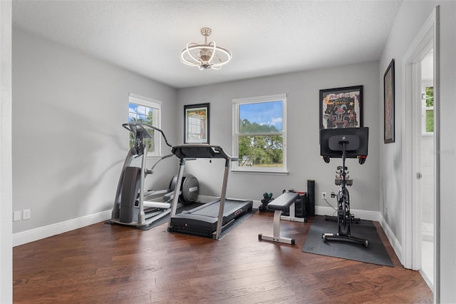 workout room featuring a chandelier, wood finished floors, baseboards, and a textured ceiling