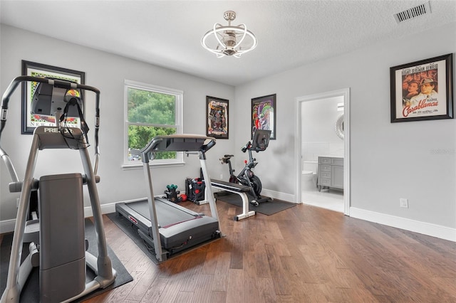 workout area featuring a chandelier, wood finished floors, baseboards, and a textured ceiling