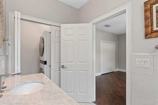 bathroom featuring estacked washer and dryer, wood finished floors, baseboards, and vanity