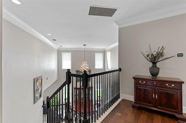 hall with dark wood finished floors, ornamental molding, baseboards, a chandelier, and an upstairs landing