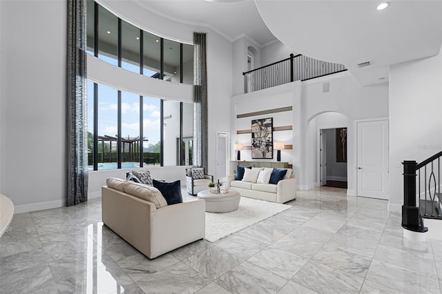 living room with arched walkways, light marble finish flooring, a towering ceiling, baseboards, and crown molding
