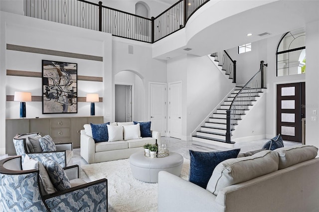 living area featuring arched walkways, a towering ceiling, baseboards, stairs, and marble tiled floors