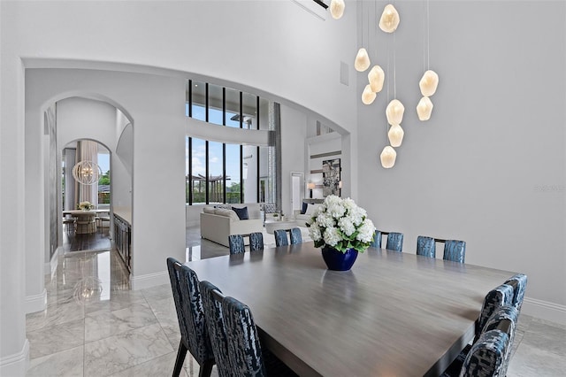 dining area with arched walkways, marble tiled flooring, a towering ceiling, and baseboards