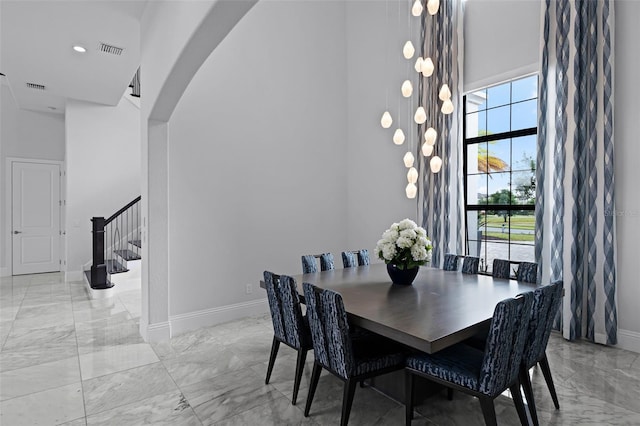 dining room with a towering ceiling, light marble finish flooring, baseboards, stairs, and arched walkways