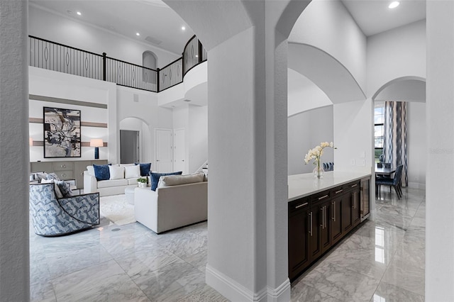hallway featuring light marble finish floors, arched walkways, a towering ceiling, baseboards, and recessed lighting
