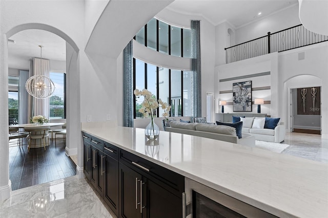 kitchen featuring arched walkways, dark cabinetry, baseboards, plenty of natural light, and a towering ceiling