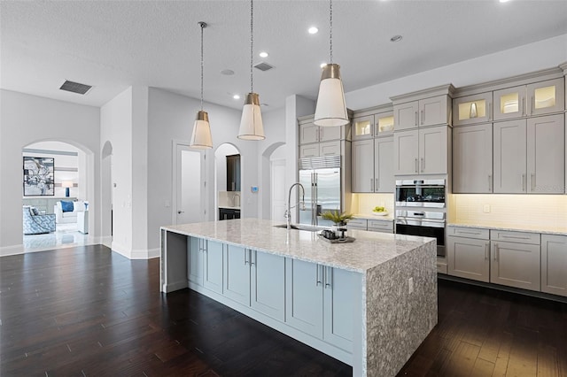 kitchen with stainless steel appliances, arched walkways, gray cabinets, a sink, and recessed lighting