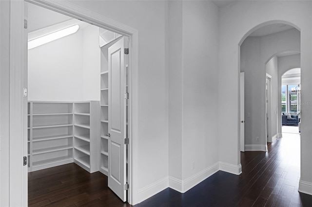 corridor featuring arched walkways, dark wood-type flooring, and baseboards