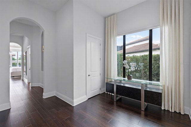 foyer entrance featuring arched walkways, dark wood-style floors, and baseboards