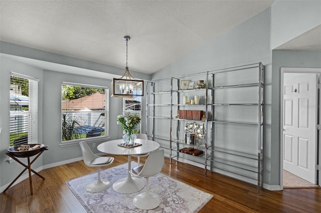 dining area featuring vaulted ceiling, wood finished floors, a chandelier, a textured ceiling, and baseboards