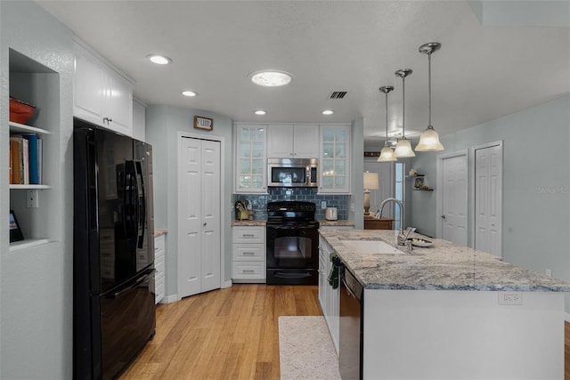 kitchen with black appliances, a sink, light wood finished floors, white cabinets, and decorative backsplash