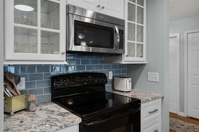 kitchen with black / electric stove, stainless steel microwave, backsplash, white cabinets, and a textured wall