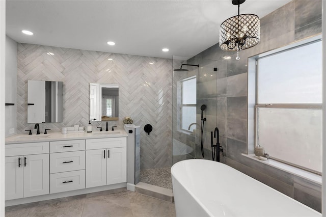 bathroom featuring a shower stall, a freestanding tub, double vanity, a chandelier, and tile walls