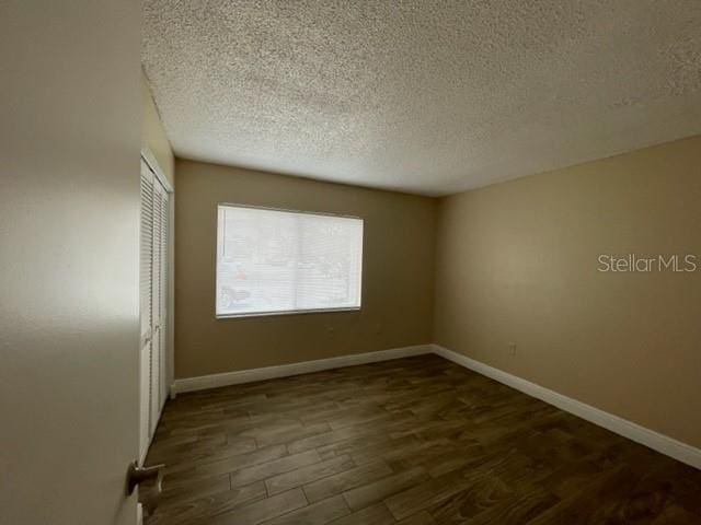 unfurnished room featuring a textured ceiling, wood finished floors, and baseboards