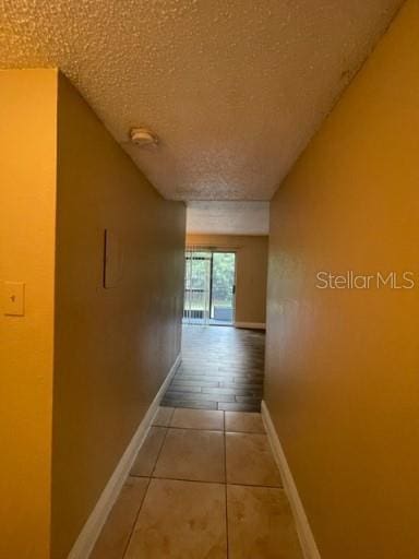 hallway featuring tile patterned flooring, a textured ceiling, and baseboards