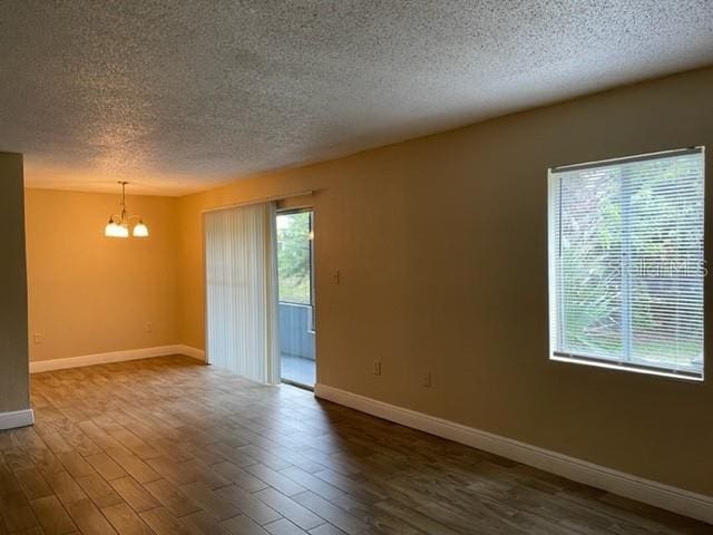 spare room with dark wood finished floors, a wealth of natural light, a textured ceiling, and a notable chandelier