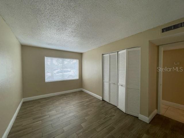 unfurnished bedroom featuring a closet, a textured ceiling, visible vents, and wood finished floors