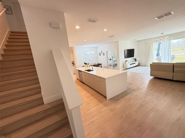 kitchen with a sink, visible vents, open floor plan, stainless steel dishwasher, and light wood-style floors
