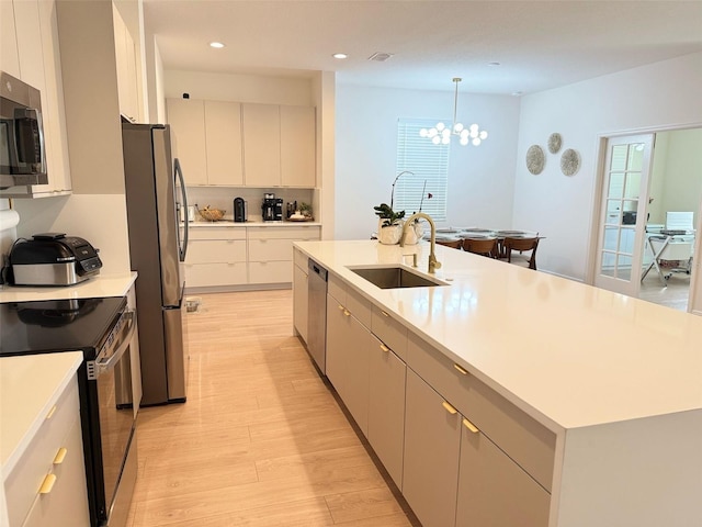 kitchen featuring a sink, stainless steel appliances, light wood-type flooring, a center island with sink, and light countertops