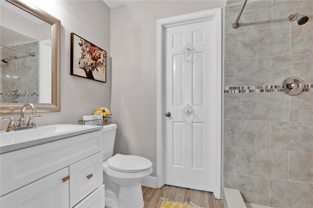 full bathroom with vanity, toilet, a tile shower, and wood finished floors