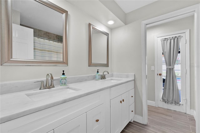 full bath featuring double vanity, wood finished floors, baseboards, and a sink