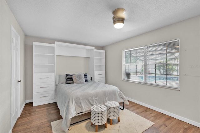 bedroom with a textured ceiling, baseboards, and wood finished floors