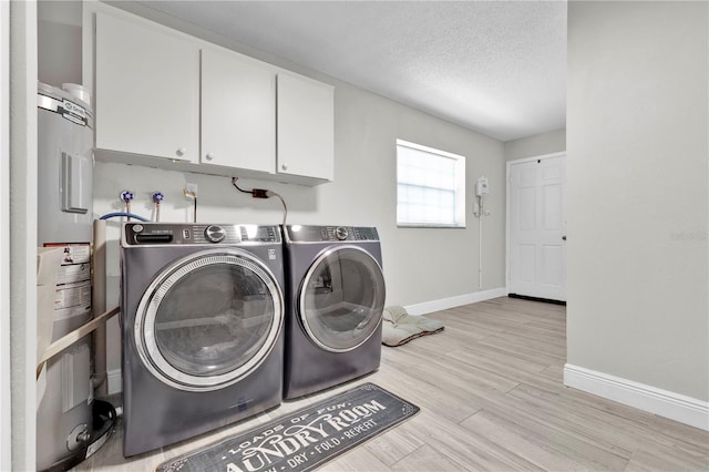 clothes washing area featuring washer and dryer, cabinet space, a textured ceiling, light wood-type flooring, and baseboards
