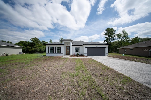 prairie-style home with an attached garage, stucco siding, decorative driveway, and a front lawn