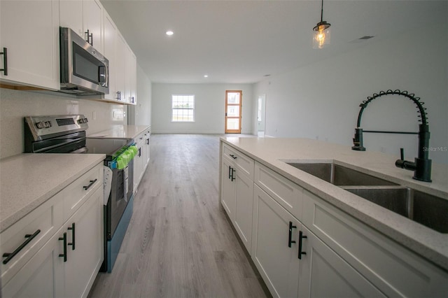 kitchen with a sink, recessed lighting, light wood finished floors, white cabinets, and appliances with stainless steel finishes