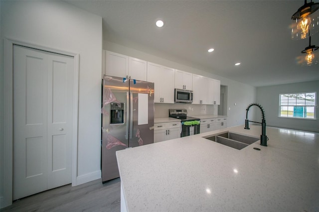 kitchen featuring wood finished floors, a sink, white cabinets, appliances with stainless steel finishes, and recessed lighting